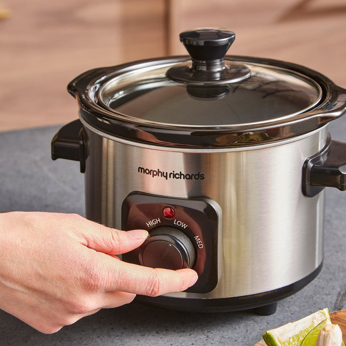 Morphy Richards slow cooker with a hand adjusting the dial on a kitchen counter.