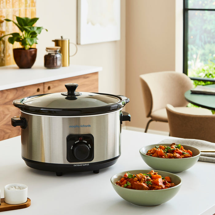 slow cooker on a kitchen counter with bowls of food next to it