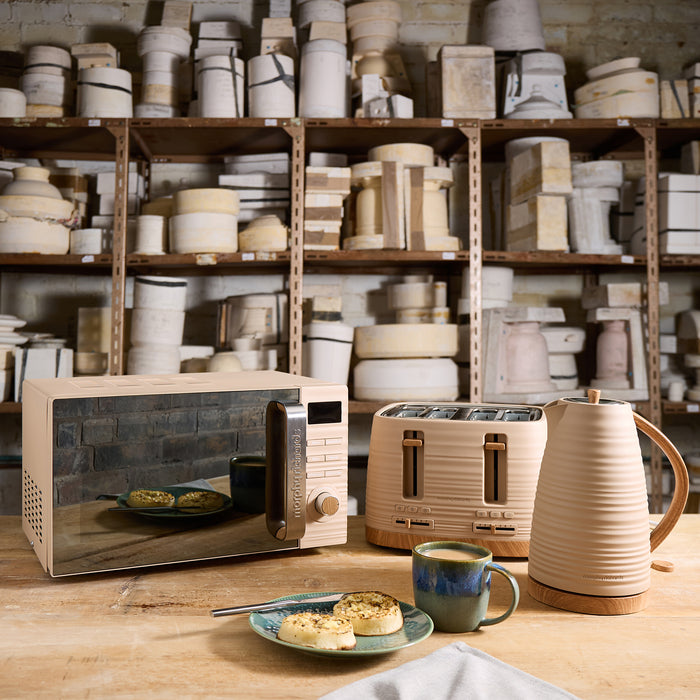 Wooden kitchen appliances including a microwave, toaster, and kettle on a wooden table with shelves of ceramic items in the background.