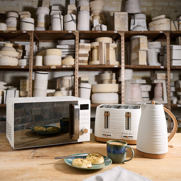 White microwave, toaster, and kettle on a wooden table with shelves of kitchenware in the background.
