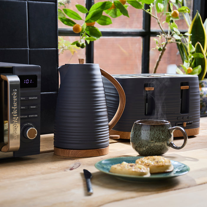 Kitchen scene with a kettle, toaster, mug, and plate of food on a wooden table.