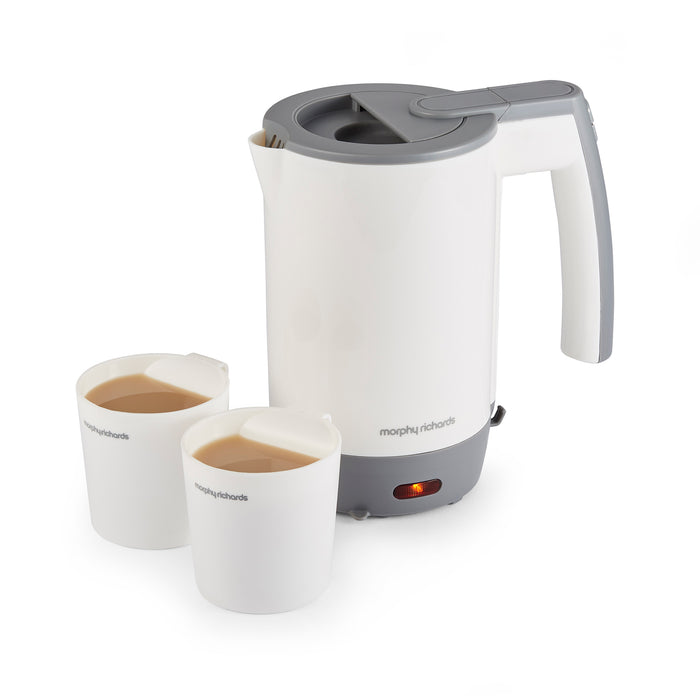A compact white Morphy Richards travel kettle with a grey hinged lid, displayed alongside two white tea cups, on a plain background.