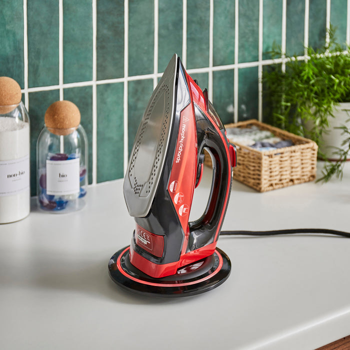 Red and black iron on a white surface with a tiled wall and plants in the background