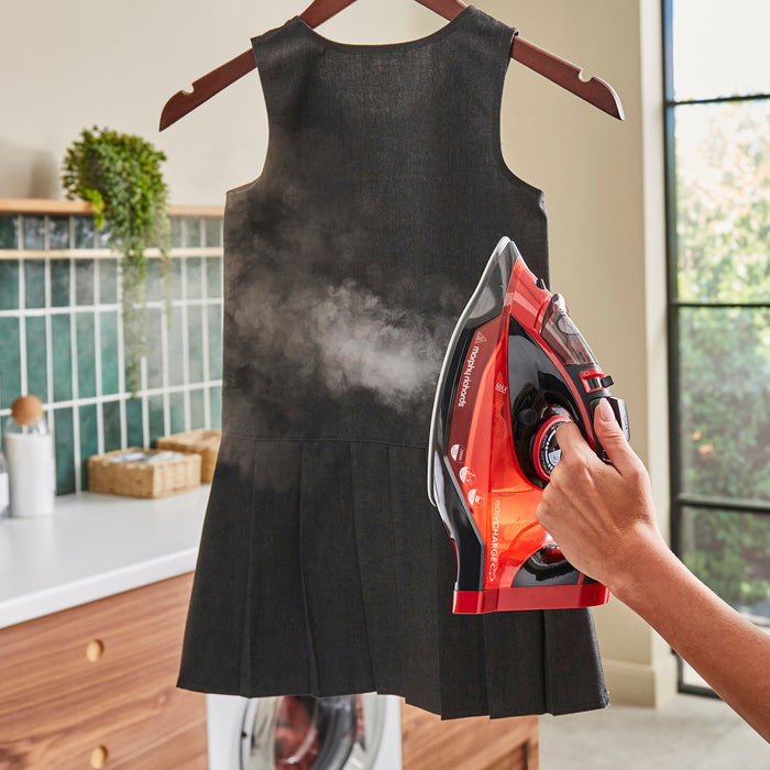 Person ironing a black dress with a red and black iron in a kitchen setting.