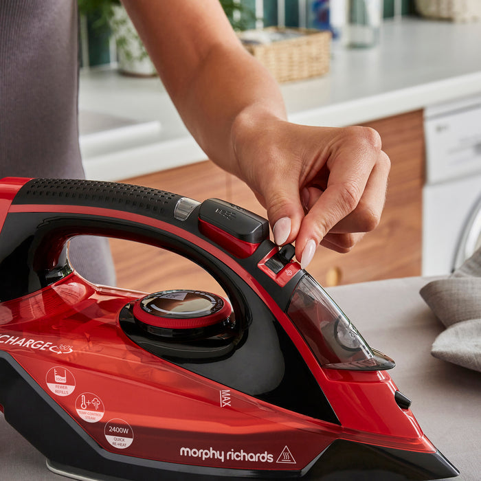 Red and black Morphy Richards iron being used by a person in a kitchen setting.