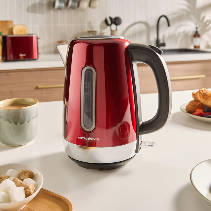 Red Morphy Richards kettle on a kitchen counter with a cup of coffee and breakfast items.