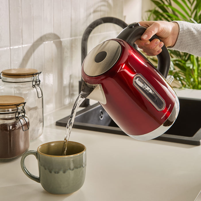 Red electric kettle being used to pour water into a green mug on a kitchen counter.
