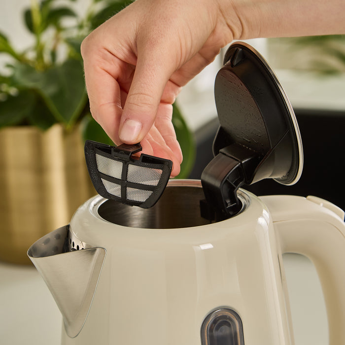 Person placing a black mesh filter into a beige kettle with a blurred plant in the background.