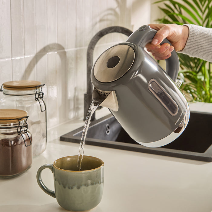 Person pouring water from a jug kettle into a mug on a kitchen counter.