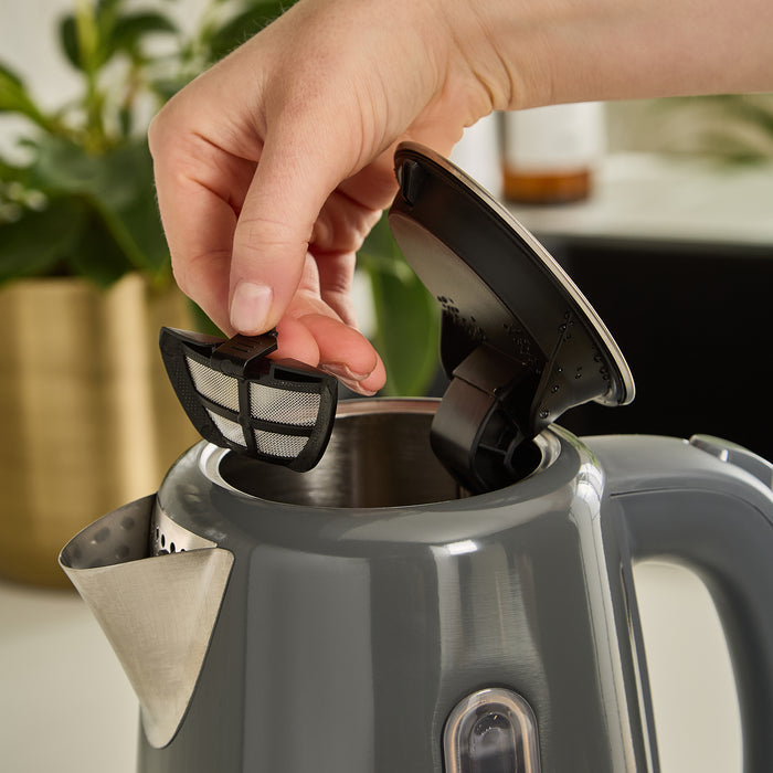 Person replacing a filter in a gray electric kettle with a blurred kitchen background