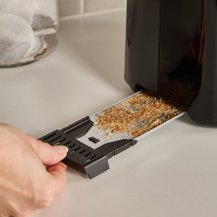 Person removing crumbs from a toaster crumb tray on a kitchen counter.