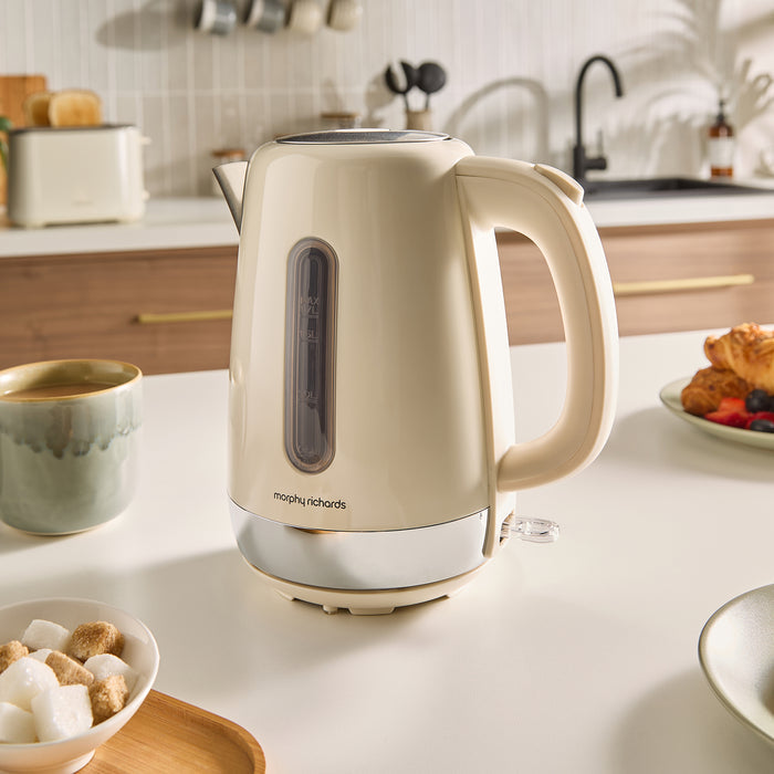 Beige kettle on a kitchen counter with a cup of coffee and breakfast items.