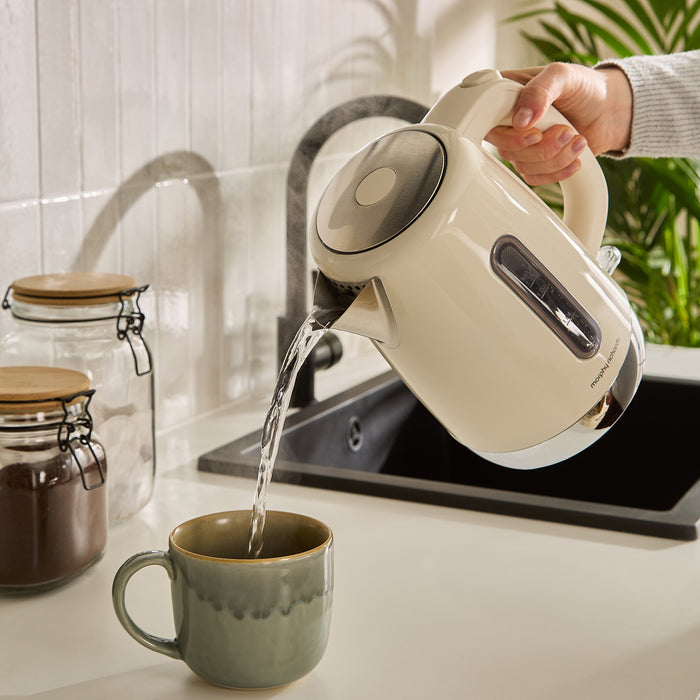 Person pouring water from a white kettle into a green mug on a kitchen counter.