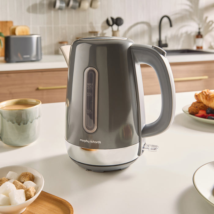 Grey jug kettle on a kitchen counter with a cup of coffee and snacks.