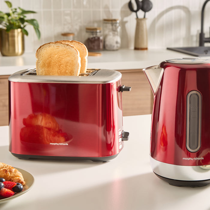 Red toaster and kettle on a kitchen counter with toast and fruit.