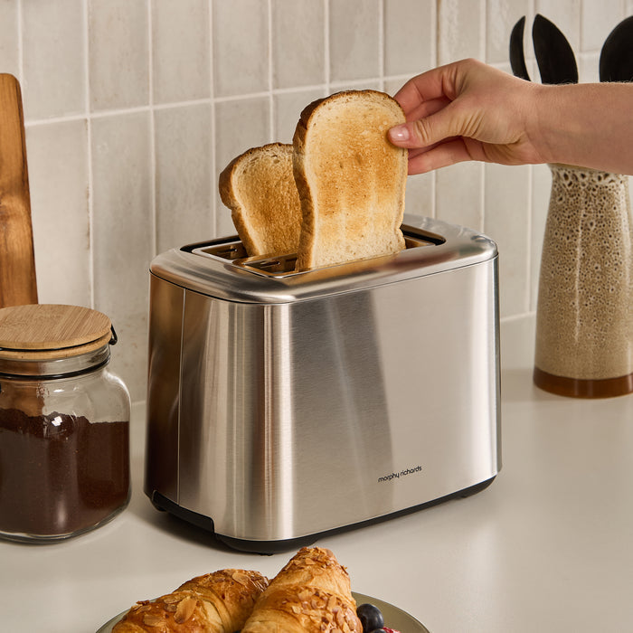 Person placing toast in a stainless steel toaster with a kitchen setting.