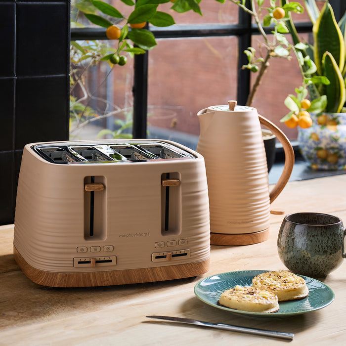 Beige toaster on a kitchen counter with a plate of toast, mug, and kettle in the background.