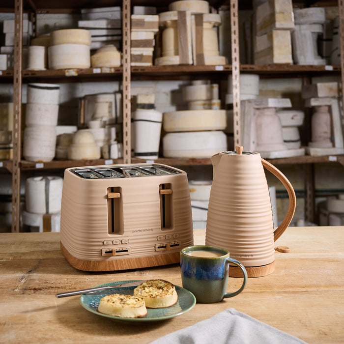 Beige toaster and kettle on a wooden table with a cup of coffee and plate of pastries, shelves with kitchenware in the background.