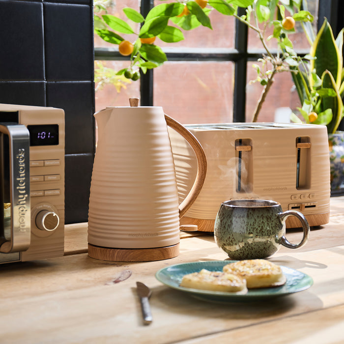 Kitchen scene with a kettle, toaster, mug, and plate of cookies on a wooden table.