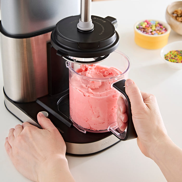 Person using a kitchen appliance to blend pink ice cream into a container.