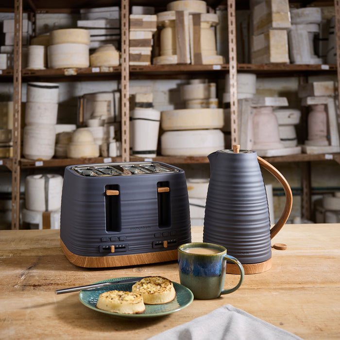 Kitchen scene with toaster, kettle, mug, and plate on a wooden table with shelves in the background.