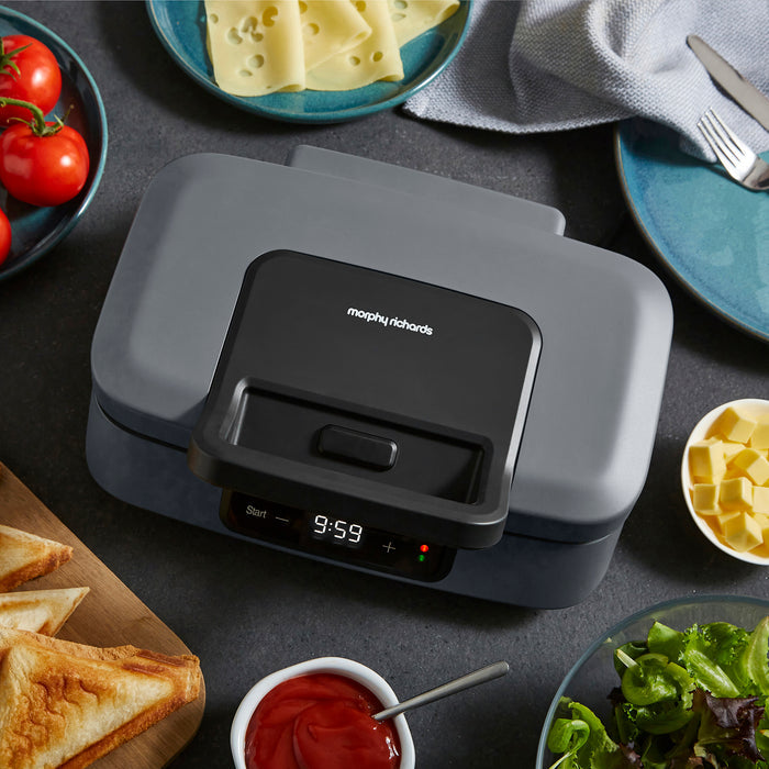 Gray sandwich maker with digital display on a kitchen counter with food items around