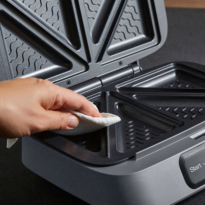 Person cleaning a sandwich maker with a cloth
