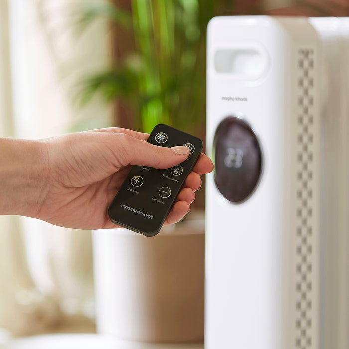 Hand holding a remote control near a white appliance with a blurred background