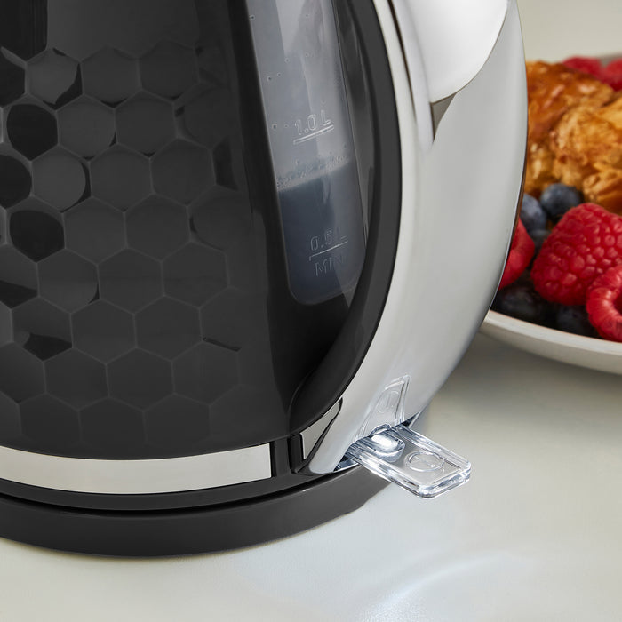 Black and silver electric kettle on a white surface with a plate of food in the background