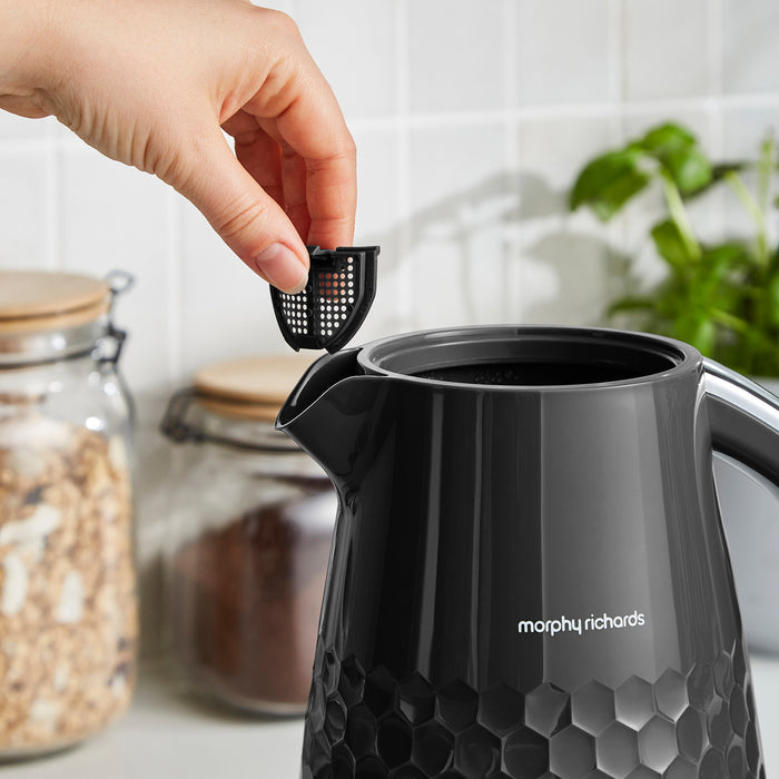 Person placing a black filter into a Morphy Richards kettle in a kitchen setting.