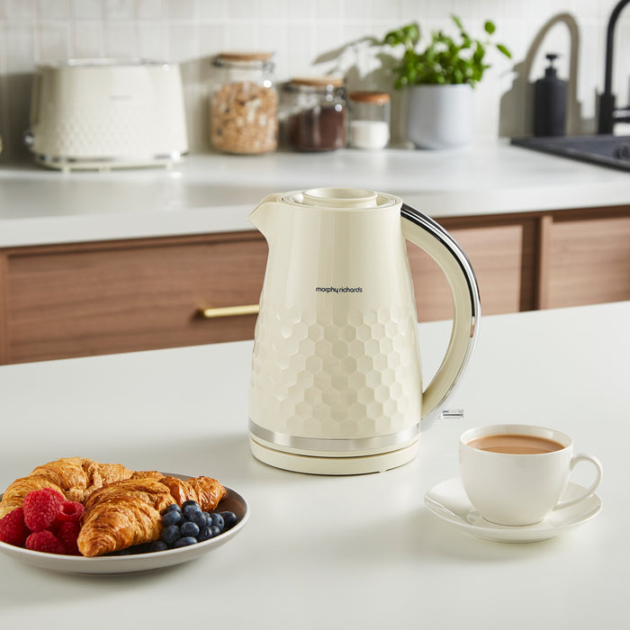 White electric kettle on a kitchen counter with a cup of coffee and a plate of pastries.