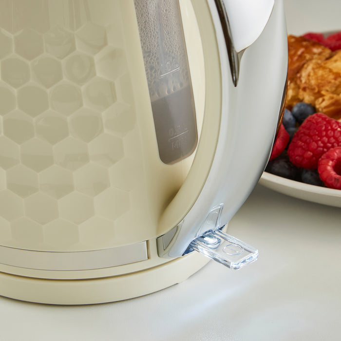 Beige electric kettle with a clear lid on a white surface, next to a bowl of berries and toast.