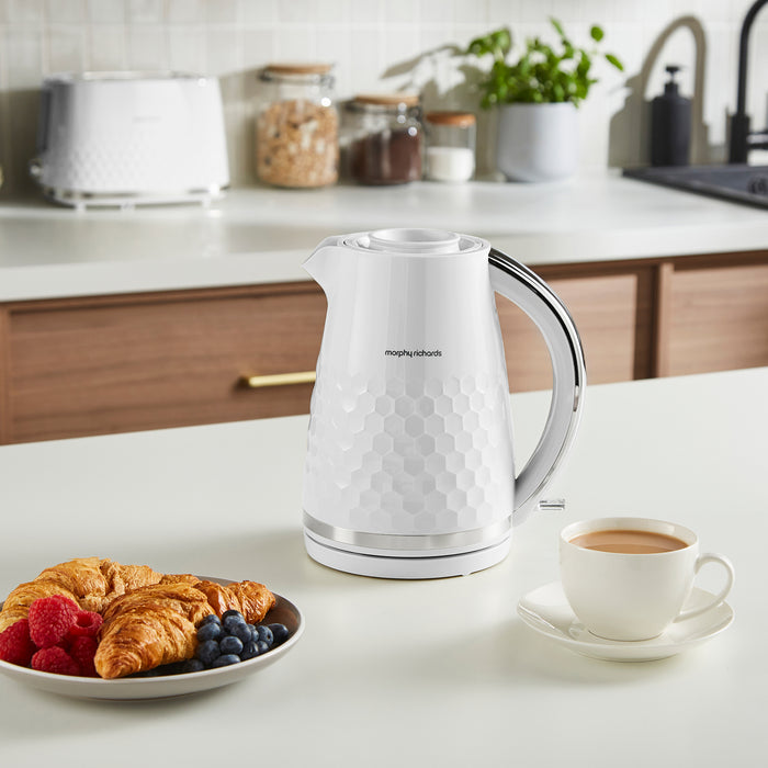 White electric kettle on a kitchen counter with a plate of pastries and a cup of coffee.