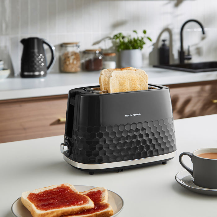 Black toaster with slices of bread on a kitchen counter with a cup of coffee and toast.