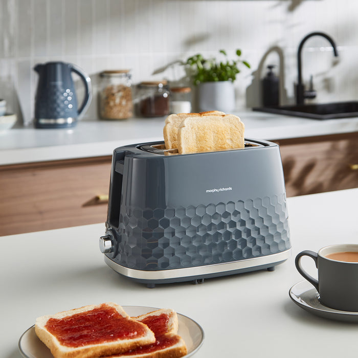 Grey toaster with slices of toast on a kitchen counter with a cup of coffee.