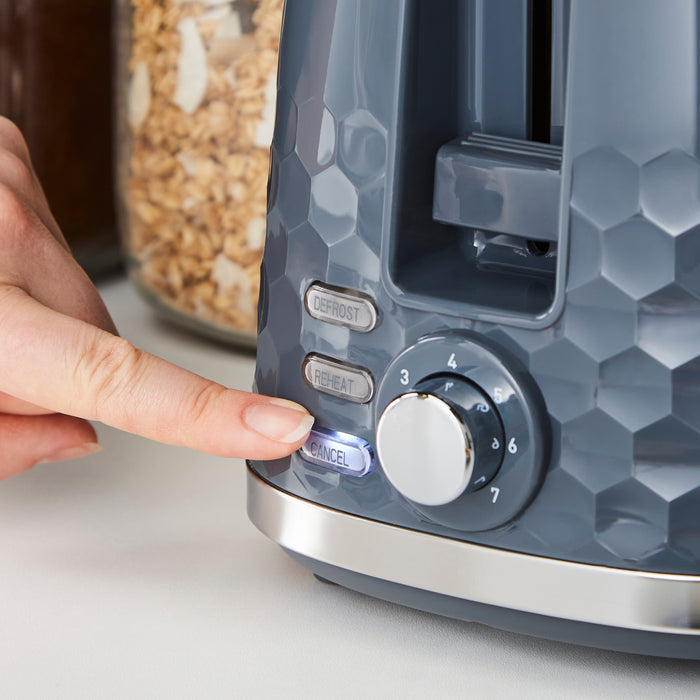 Person adjusting a knob on a blue toaster with a jar of granola in the background.