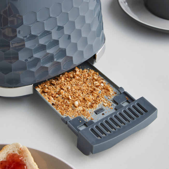 Grey toaster with crumb tray filled with crumbs on a white surface.