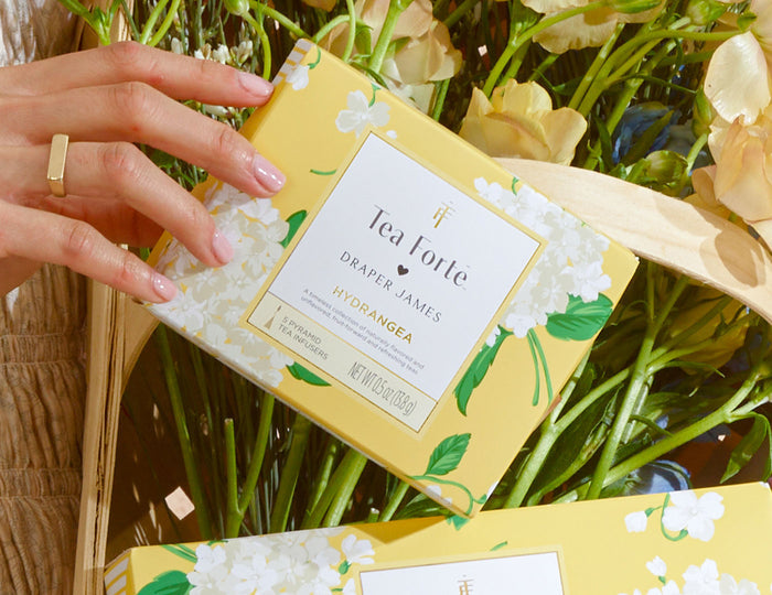 MAIN PDP | Tea Forte Draper James Hydrangea Mini Peite box held by a hand with flowers in the background