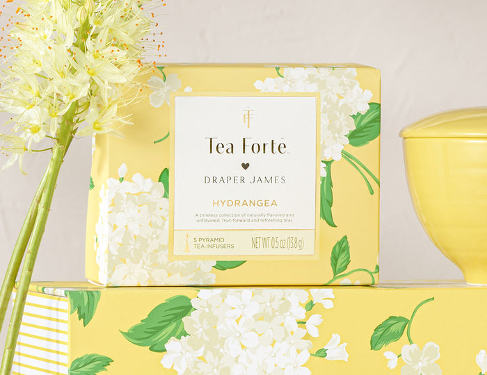 Yellow presentation box with white hydrangea flowers and green leaves, containing Tea Forte tea infusers.