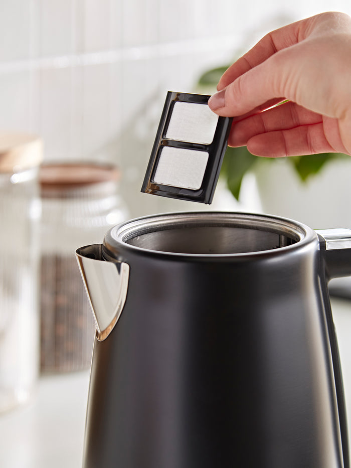 Person placing a black coffee filter into a silver kettle.
