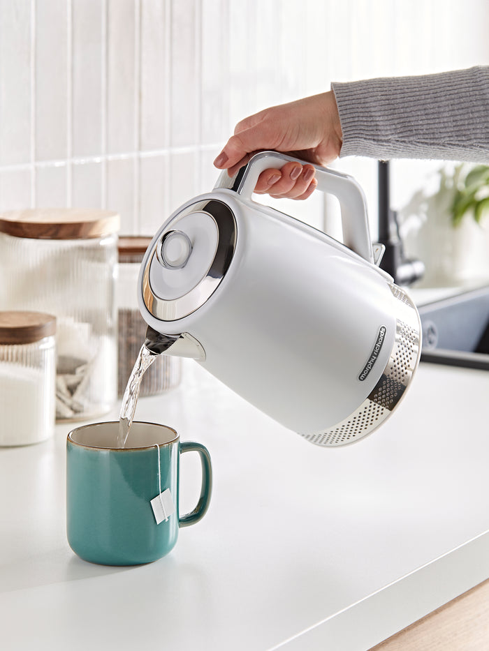 White electric kettle being used to pour water into a blue mug on a kitchen counter.