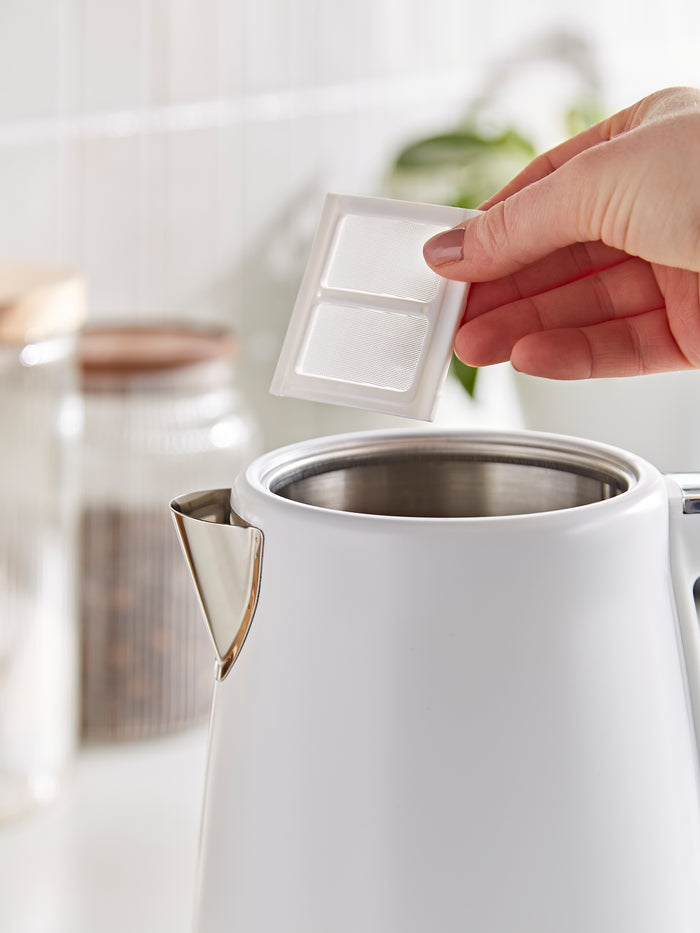 Person holding a filter above a white electric kettle.