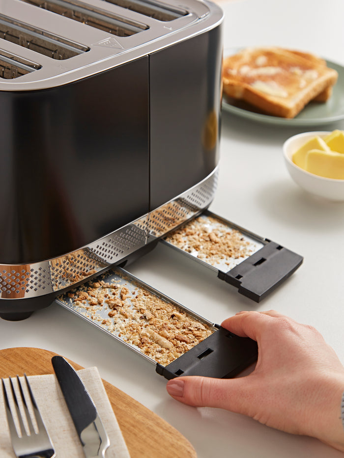 Toaster with crumb tray being pulled out, surrounded by breakfast items on a table.