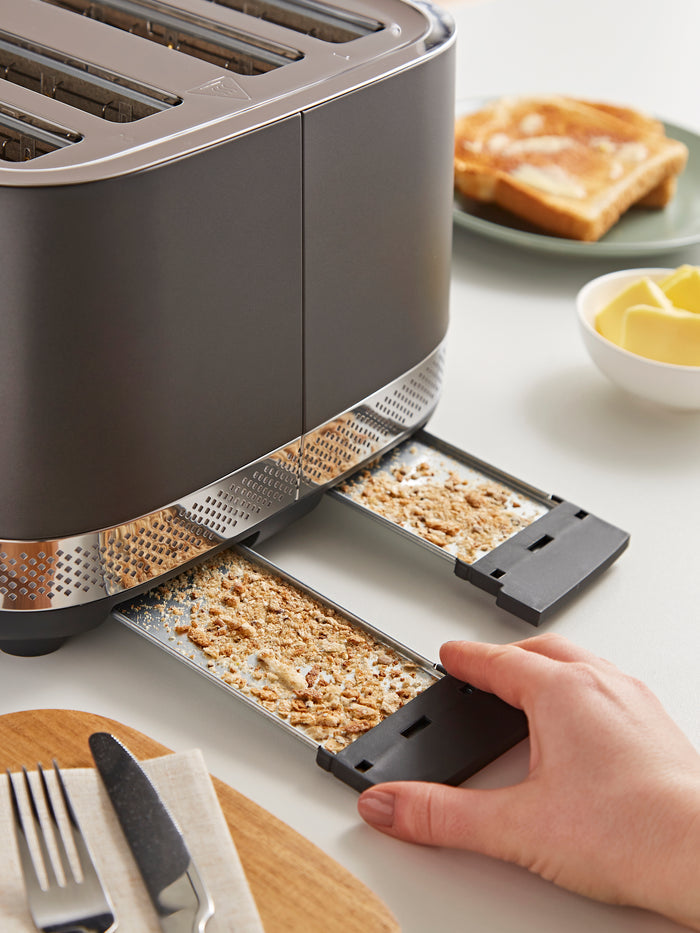 Gray toaster with crumb tray on a kitchen counter, next to a plate of toast and butter.