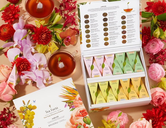 MAIN PDP | Jubilee Tea Chest of 40 pyramid tea infusers on table among flowers and teacups, open and closed boxes