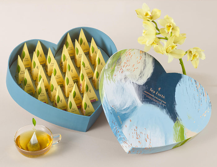 MAIN PDP | Keepsake Heart Box, Something Blue, of 26 pyramid infusers, lid open, revealing infusers, with cup of tea and flowers