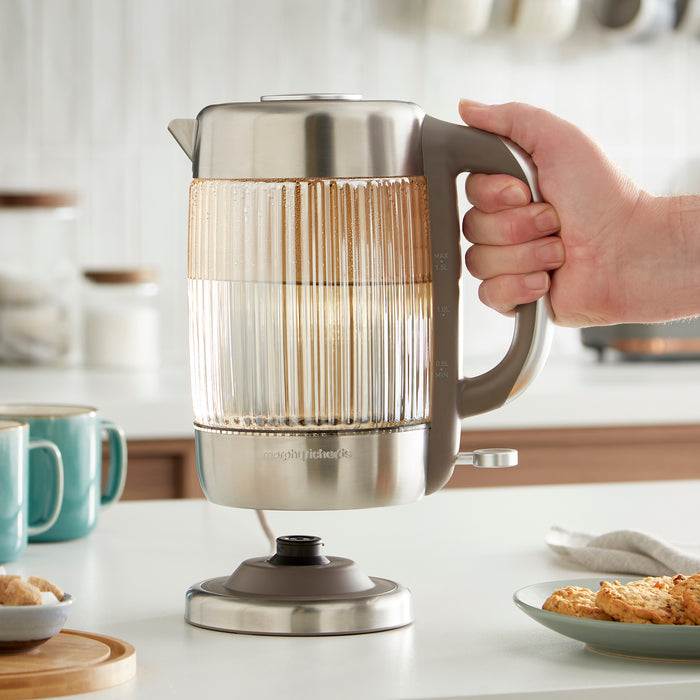Person holding a stainless steel electric kettle on a kitchen counter.
