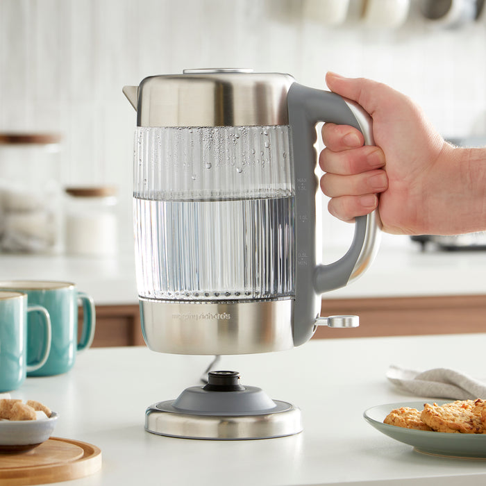 Person holding a stainless steel electric kettle on a kitchen counter.