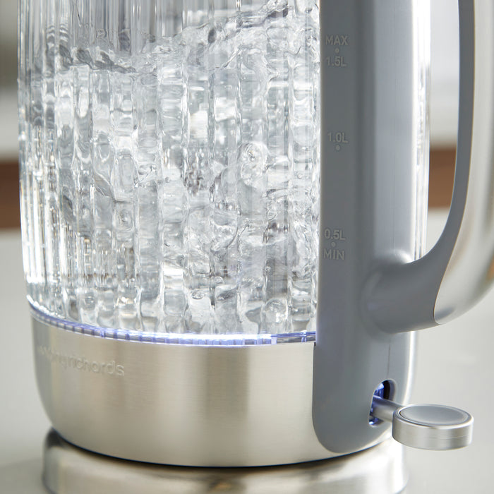 Clear glass electric kettle with ice cubes inside on a neutral background