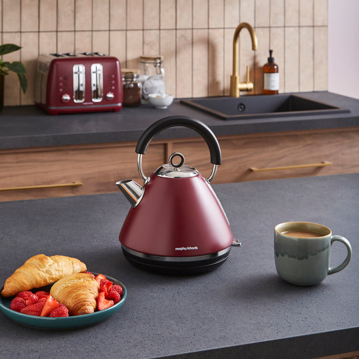 Red kettle on a kitchen counter with a mug and plate of food.